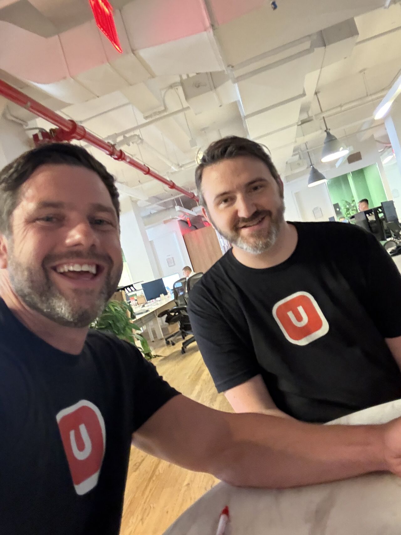 Bob and Kilty, the two founders of Unfairly, in the office wearing Unfairly t-shirts.